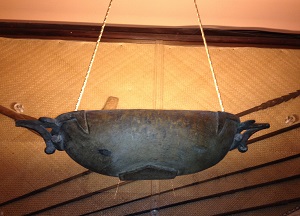 Rope suspended boat serving bowl lamp in front of Polynesian reed mat and fishing spears