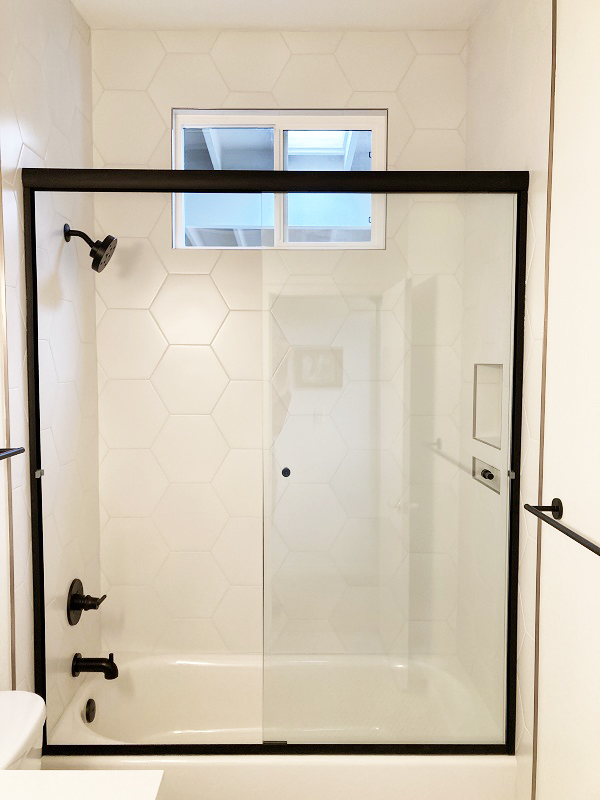 Glass sliding shower doors with frame on tub.