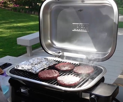 Hamburgers and foil wrapped asparagus on the Weber Lumin electric outdoor grill.
