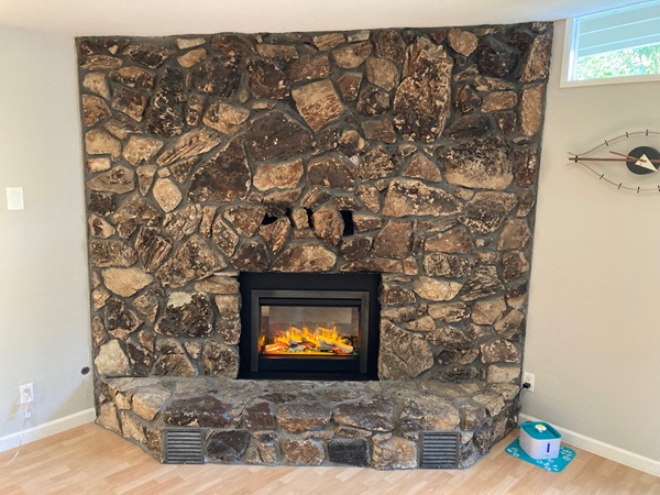 New electric fireplace insert operational surrounded by the Mexican driftwood stone wall and hearth.