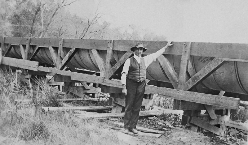 Undated photo of a man standing next to a half-pipe metal flume of the North Fork Ditch. Unknown if the man is Loring Jordan.